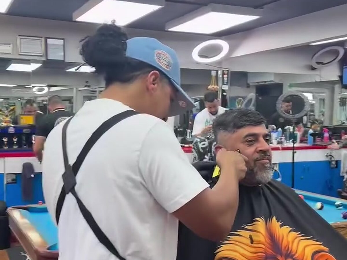A barber lining up a client beside the shop pool table